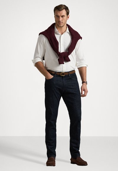 Λευκό πουκάμισο με κουμπιά, σκούρο μπλε τζιν, μπορντό πλεκτό πουλόβερ δεμένο στον λαιμό, καφετί ζώνη και καφετιά παπούτσια. Απλή, κλασική casual εμφάνιση.