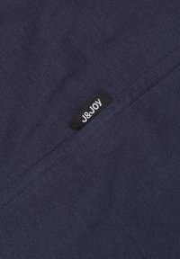 Marineblauwe stof met een gestructureerd oppervlak heeft een zwart label met de tekst "J&Joy" in witte letters. Eenvoudig, schoon ontwerp.