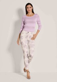 Licht paarse gebreide trui met ribbeltextuur, gecombineerd met crèmekleurige broek met bloemenprint en paarse accenten in een aansluitend ontwerp. Zwarte sandalen met hakken.