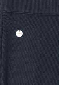 Tissu côtelé bleu foncé avec une petite étiquette ronde argentée indiquant le nom de la marque Street One, cousue près d'une couture.