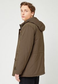 Giacca imbottita marrone con cappuccio, dotata di zip frontale e tasche laterali, realizzata in un tessuto liscio e resistente. Design semplice e funzionale.