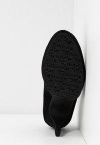 Chaussure à talon haut en daim noir avec un bout pointu et une semelle texturée portant le nom de la marque en relief. Tige lisse et talon fin.