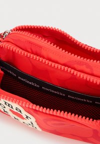 Κόκκινη θήκη με φερμουάρ με πολλαπλά διαμερίσματα, εσωτερική μαύρη τσέπη από δίχτυ και διακοσμητική ταινία υφάσματος με την επωνυμία «marimekko».