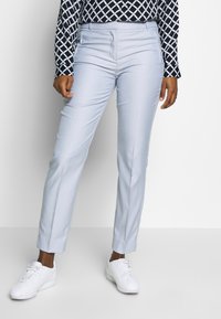 Pantalons sur mesure bleu clair avec une texture lisse, dotés de poches latérales et d'une coupe slim, associés à des baskets blanches et un haut à motifs.