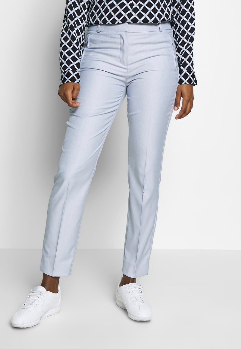 Pantalons sur mesure bleu clair avec une texture lisse, dotés de poches latérales et d'une coupe slim, associés à des baskets blanches et un haut à motifs.