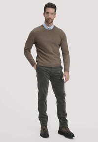 Brauner Wollpullover, hellblaues Hemd mit Kragen, dunkelgrüne Cordhosen und braune Stiefel, mit einer taillierten Silhouette und strukturierten Materialien.