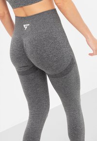 Szare legginsy z wysokim stanem, wykonane z teksturowanej tkaniny z logo na plecach, charakteryzujące się dopasowanym krojem i subtelnymi akcentami stylistycznymi.