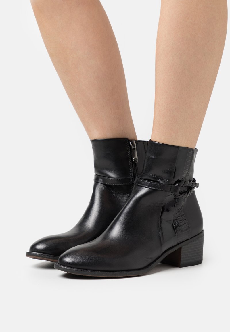 Bottes noires à chevilles en cuir lisse avec une fermeture éclair sur le côté, un léger talon et un détail de bride tressée décoratif. Accents texturés sur le côté.