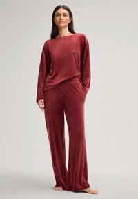 Ensemble de loungewear en velours rouge profond, comprenant un haut à manches longues avec une coupe décontractée et un pantalon large assorti avec des poches latérales.