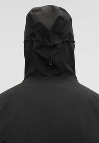 Čierna vodeodolná bunda s kapucňou a sťahovacou šnúrkou, hladkou textúrou látky a minimalistickým dizajnom. Žiadne viditeľné kovanie ani vzory.