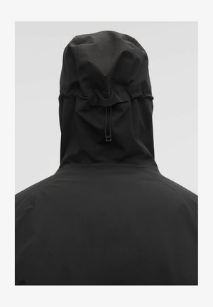 Melnas ūdensnecaurlaidīgas jakas ar kapuci un auklu, gluda auduma tekstūra un minimālisma dizains. Nav redzamu aparatūras vai rakstu.