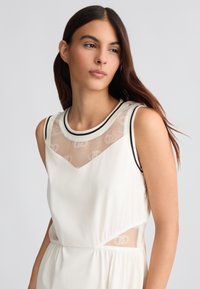 Abito bianco senza maniche con un pannello trasparente decorato da un motivo a logo, rifiniture nere attorno al collo e una linea del tessuto fluida.