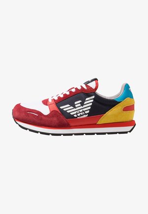 Zapatilla deportiva roja, blanca, negra, amarilla y azul con un gran logo blanco de águila en el lateral y cordones blancos, vista desde el lado exterior.