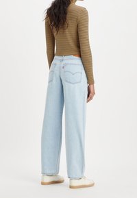 Ljusblå vida jeans med hög midja, som har två bakfickor och en märkeslapp i läder vid midjan.