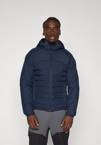 Veste rembourrée bleu marine avec capuche, dotée de poches latérales zippées et de sections texturées sur le devant pour l'isolation.