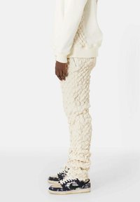 Crème-kleurige textuur broek met een unieke verhoogde patron, gecombineerd met zwart-beige sneakers met een paisleypatroon.