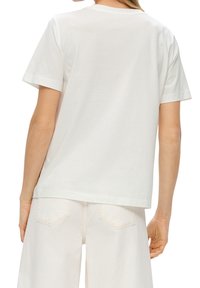 Hvid bomulds t-shirt med korte ærmer, rund halsudskæring og en afslappet pasform, vist fra ryggen mod lysfarvede bukser.