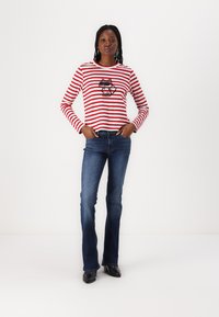 Red and white striped long-sleeve shirt with a black animal graphic, paired with blue flared jeans and black footwear.