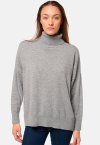 Pull en col roulé gris avec une coupe décontractée, une texture douce, des épaules tombantes, des poignets et un ourlet côtelés. Porté avec un jean foncé.