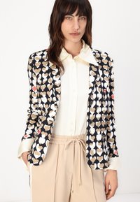 Blazer met een zwarte achtergrond met een hartpatroon in beige en wit. Twee knopen sluiting, notch revers en lange mouwen.