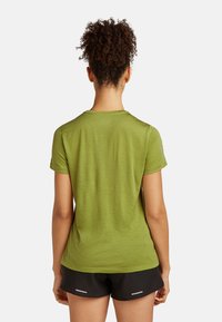 Zielona koszulka sportowa z dopasowanym krojem, krótkimi rękawami i teksturowanym materiałem; zestawiona z czarnymi szortami z odblaskowymi akcentami.