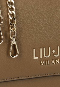 Bolso de cuero marrón con superficie texturizada, correa de cadena en tono dorado y logo de la marca en relieve. Cierre sencillo visible.