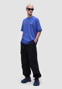 Królewsko-niebieska bawełniana koszulka, luźny krój, w połączeniu z czarnymi spodniami cargo z kieszeniami bocznymi, uzupełniona niebiesko-czarnymi trampkami.