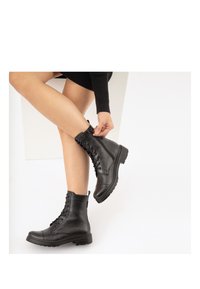 Stivali alla caviglia in pelle nera con punta rotonda, allacciatura frontale e lato testurizzato. Presentano un tassello sul retro e una suola in gomma spessa.