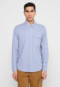 Lichtblauw button-up shirt met lange mouwen, van katoen, met een enkele borstzak en witte knopen, gedragen met beige cargobroeken.