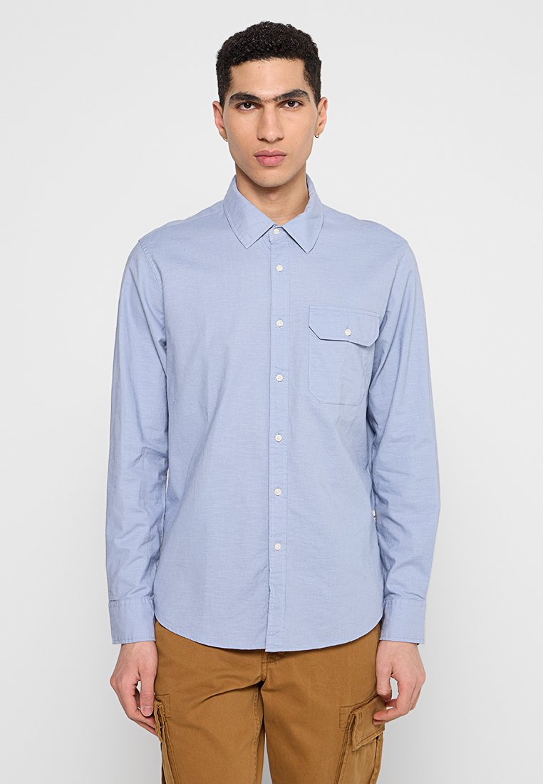 Lichtblauw button-up shirt met lange mouwen, van katoen, met een enkele borstzak en witte knopen, gedragen met beige cargobroeken.