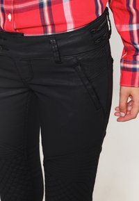 Svarta jeans med texturerade detaljer och framträdande sömmar. Har en slät midjeband med dragkedjefickor.