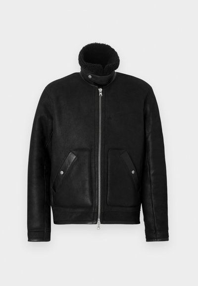 Juoda odinė striukė su aukšta apykakle ir užtrauktuku. Turi du priekinius kišenes su atlapo detalėmis. Lygi tekstūra su matinio paviršiaus apdaila.