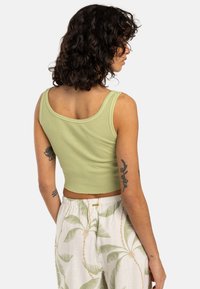 Light green ribbed crop tank top with wide straps. The back features a rounded neckline and a fitted design. Paired with patterned pants.