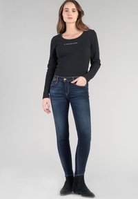 Top negro de manga larga con relieve y escote redondo. Vaqueros ajustados azul oscuro con cinco bolsillos y costuras claras. Combinado con botas negras de tobillo.