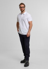 Witte poloshirt met een kraag en korte mouwen, gecombineerd met donkerblauwe broek en zwarte enkellaarsjes. Eenvoudig ontwerp met minimale accenten.