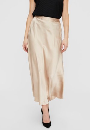 Kvinde iført en high-waist midi-nederdel i champagnefarvet satin kombineret med sort ærmeløs top og sorte spidse hæle på hvid baggrund.