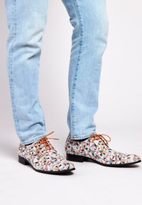 Multicolored patterned shoes featuring geometric shapes in black, white, orange, and red, with brown laces and a low, flat heel.