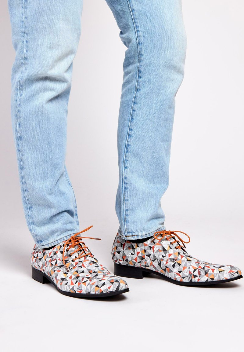 Multicolored patterned shoes featuring geometric shapes in black, white, orange, and red, with brown laces and a low, flat heel.