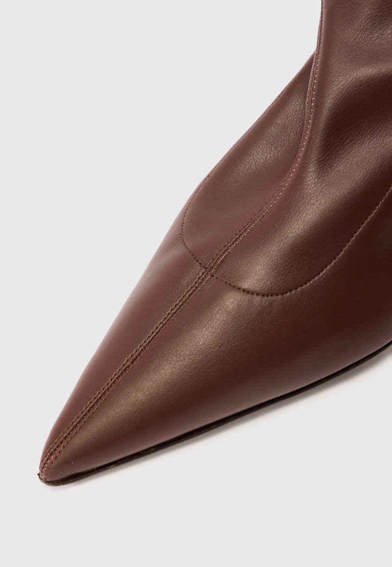 Brun lädersko med spetsig tå, centralsöm och slät yta mot en vit bakgrund.