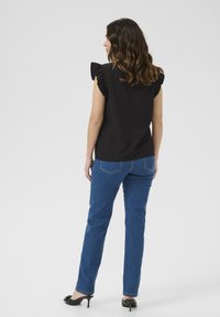 Sort, ribbet top med flæser ved skuldrene, parret med blå lige jeans og sorte højhælede sko, set fra ryggen.