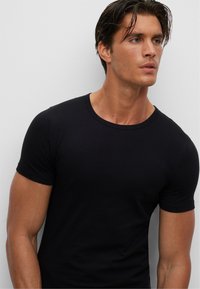 Schwarzes T-Shirt mit kurzen Ärmeln, aus einem glatten, enganliegenden Stoff mit Rundhalsausschnitt und minimalen Details, das ein klassisches Design präsentiert.