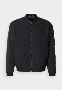 Blouson bomber noir avec fermeture éclair devant, poignets, col et taille en maille côtes, avec une poche zippée sur la manche gauche et une boucle intérieure orange.