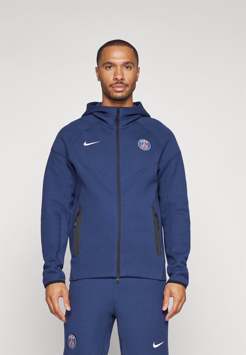 Felpa con zip di colore blu navy, con cappuccio, dotata di tasche con zip nere e un logo sul petto, realizzata in tessuto testurizzato.