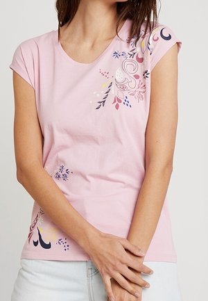 Frau trägt ein hellrosa Kurzarmshirt mit abstrakten Blumen- und Blattmustern in Blau, Lila, Gelb und Weiß.