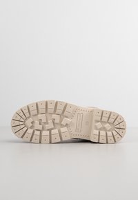 Semelle de chaussure beige avec des crampons profonds, des motifs carrés et rectangulaires, le nom de la marque "Tom Tailor" et la taille 37 marquée au centre de la semelle.