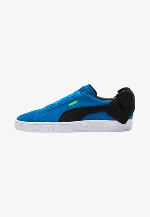 Blaue Wildledersneaker mit schwarzen Akzenten, weißer Gummisohle und einem einzigartigen schwarzen Schleifendetail an der Ferse. Mit Schnürdesign und Logo.