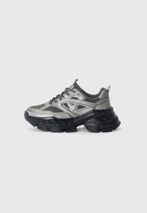 Silver and black athletic shoes with a chunky sole, mesh panels, and curved design. Features laces and a pull tab at the heel.