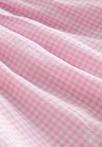 Roza gingham tkanina s uzorkom mreže. Mekana tekstura s laganim sjajem, s blagim naborima koji stvaraju suptilne valove. Glatka površina.