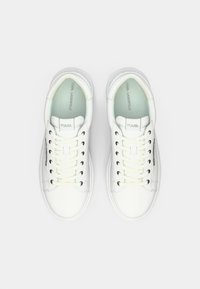 Balti odiniai sportbačiai su apvaliais nosimis, plokščiomis raištelėmis ir glotnia tekstūra. Yra logotipas ant liežuvėlio ir akcentai šone.