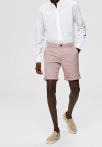 Shorts en lin rose clair avec des ourlets retournés, associés à une chemise blanche à boutons texturée et des chaussures à enfiler beiges.